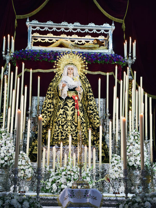 Estandarte de la Virgen María con velas y flores en un altar festivo, iluminado con velas y adornado con flores blancas y azules.