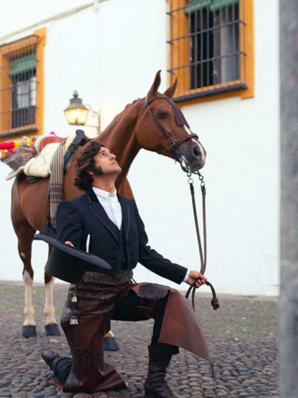 Hombre en traje tradicional andaluz posando con un caballo en una calle adoquinada.