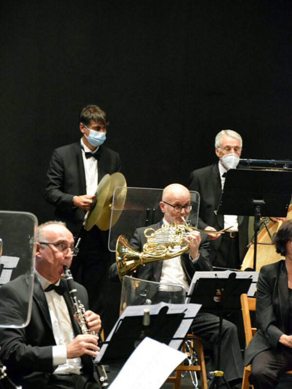Orquesta en concierto con músicos tocando instrumentos de viento y percusión.