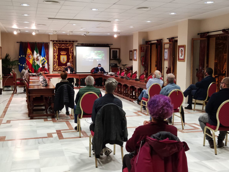 Reunión en un salón de actos con personas sentadas en filas, escuchando a un hablante en el centro.