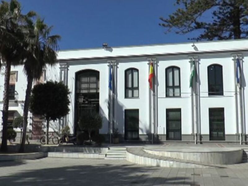 Edificio blanco con banderas y árboles en un entorno urbano.