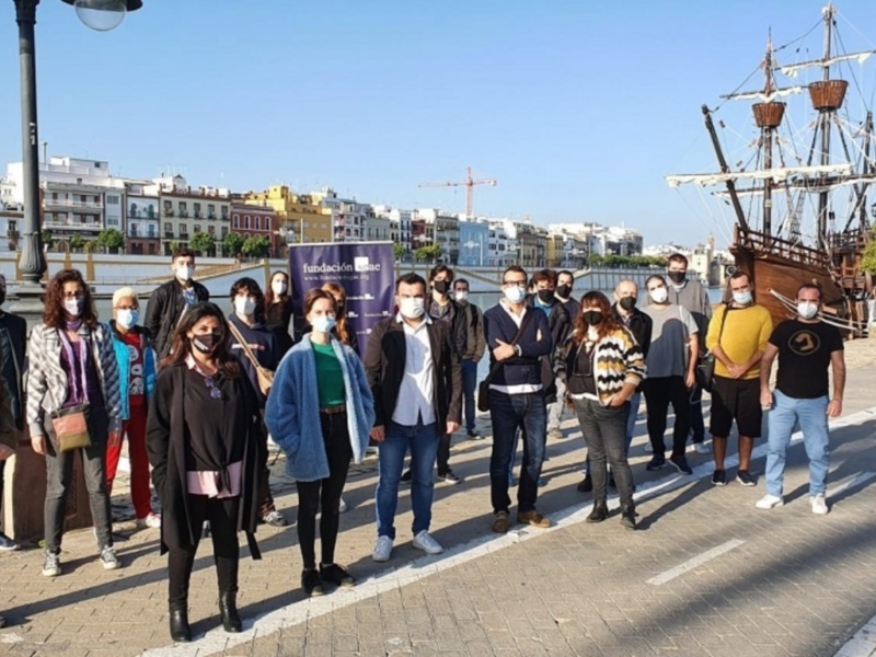 Grupo de personas con mascarillas posando frente a un barco de vela en un entorno urbano junto al río Guadalquivir en Sevilla.