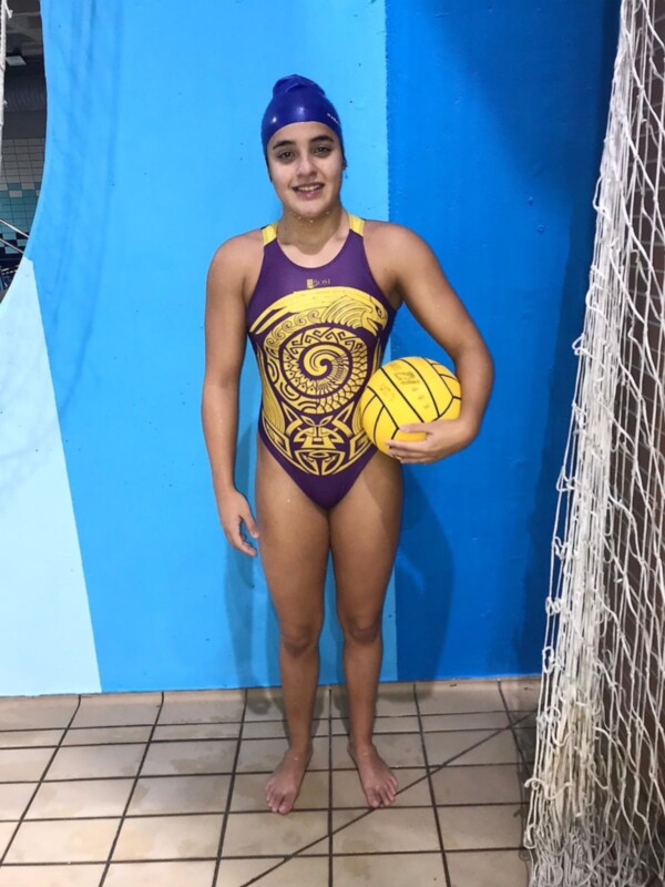 Una nadadora posa con una pelota de waterpolo en una piscina indoor.