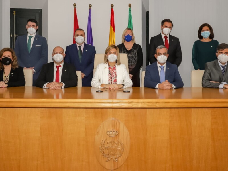Grupo de personas en una reunión formal, todos con mascarillas, frente a una mesa con el escudo de la institución.