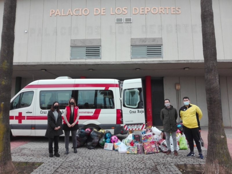 Voluntarios de Cruz Roja frente a un palacio de deportes, junto a una ambulancia y donaciones de juguetes.