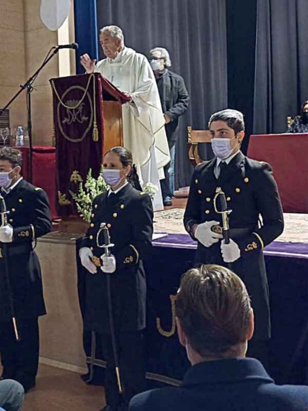 Un acto ceremonial con un sacerdote oficiando frente a estudiantes uniformados.