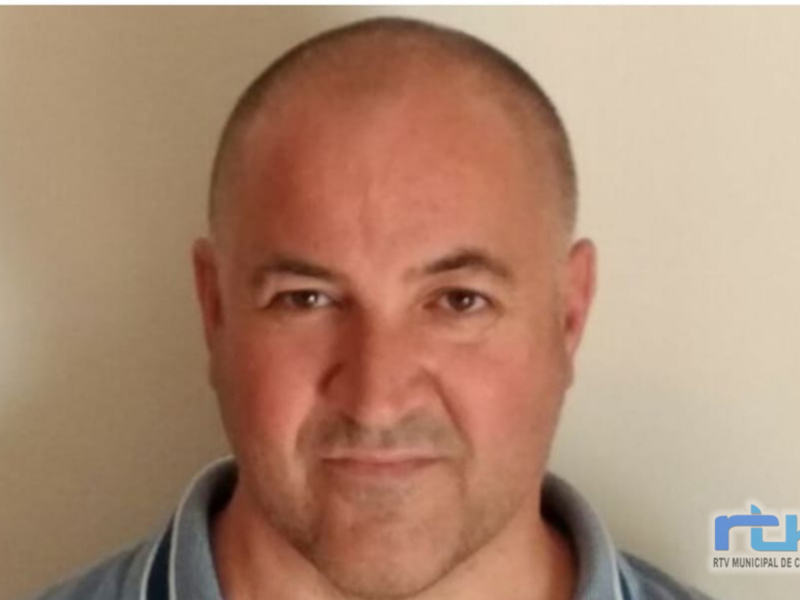 Retrato de hombre con cabello corto y camisa azul, fondo neutro.