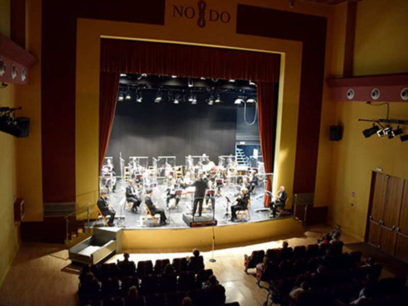 Orquesta en escenario con público en sala de conciertos.