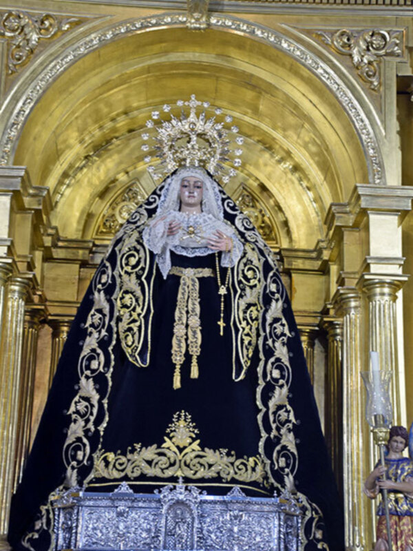 Imponente imagen de la Virgen María en un trono dorado y negro, adorada en un templo de estilo barroco.