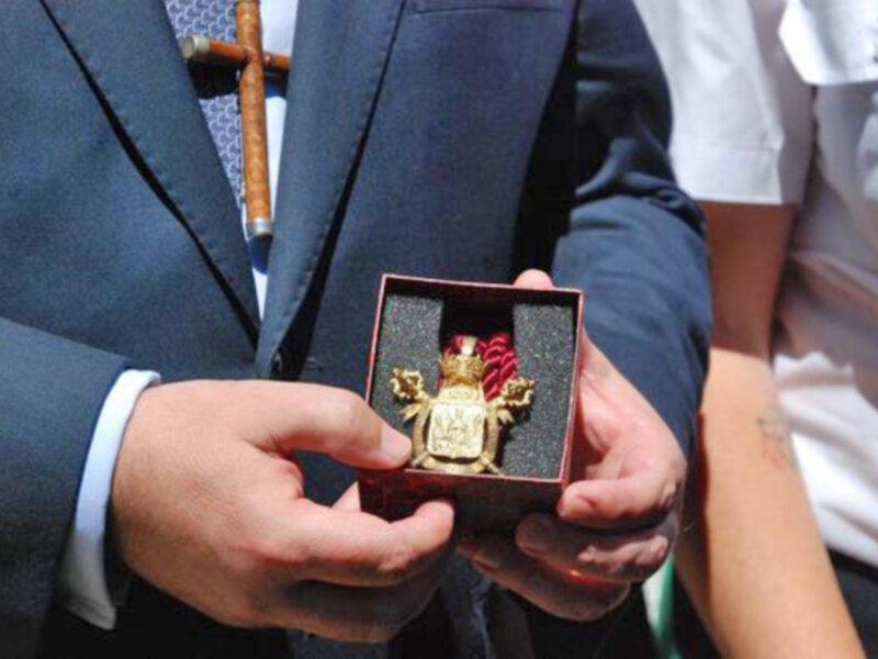 Persona sosteniendo una insignia dorada en una caja roja, simbolizando un reconocimiento o premio.