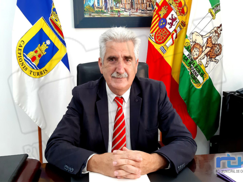 El alcalde de Chipiona, sentado en su despacho con la bandera de Cádiz y el escudo del municipio al fondo.