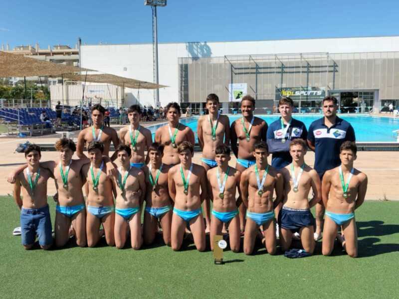 Equipo de natación juvenil con medallas posando junto a la piscina.