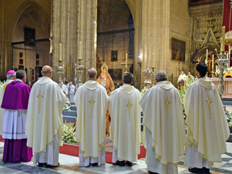 Eucaristía en una catedral, sacerdotes en hábitos blancos y un altar con ornamentos dorados.