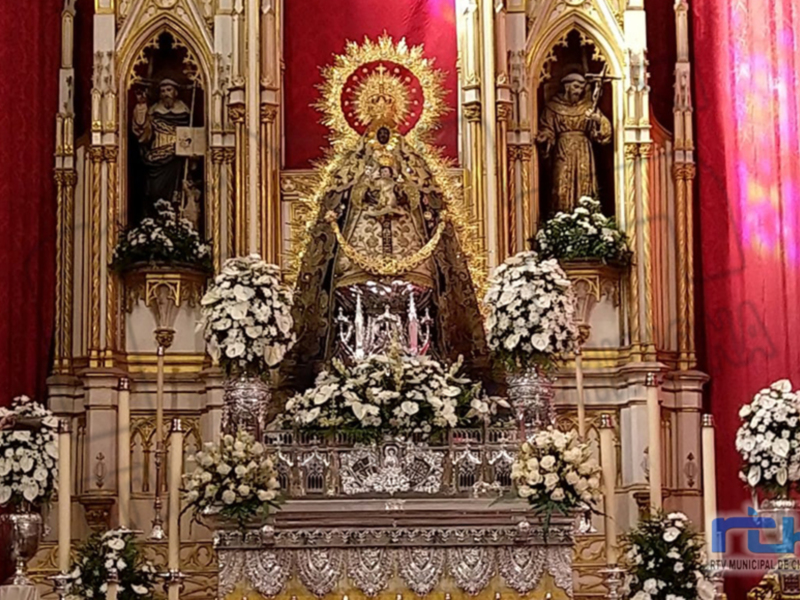 Altar ornado con flores blancas y estatuas religiosas en un entorno de color rojo y dorado.