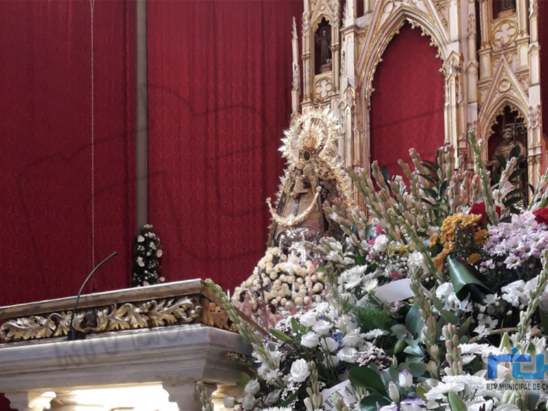 Altar de una iglesia con flores y un altar dorado en el fondo, rodeado por una cortina roja.