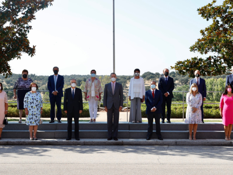 Grupo de personas posando en una ceremonia formal, todos con mascarillas, en un entorno verde con árboles y un cielo claro.