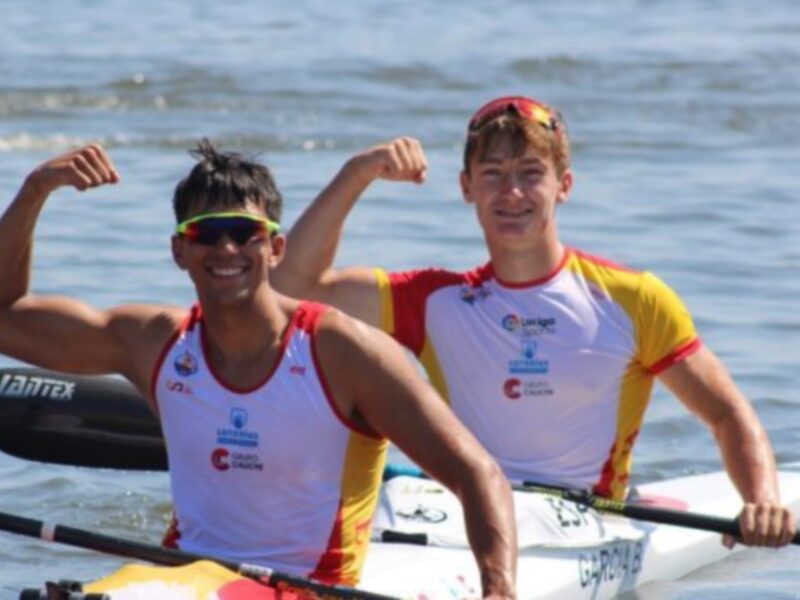 Dos atletas celebran en un kayak, con remos y fondo de agua en el fondo.