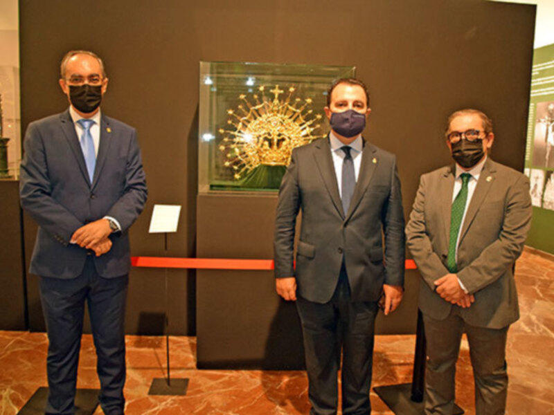 Tres hombres en trajes y mascarillas en un museo, frente a una exposición de artefactos antiguos.