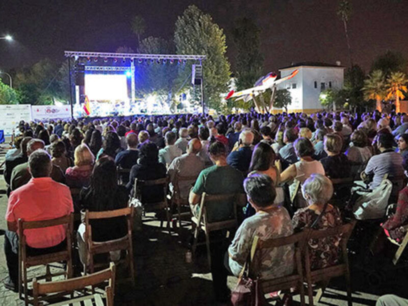 Evento nocturno con audiencia sentada en sillas frente a una escenografía iluminada.