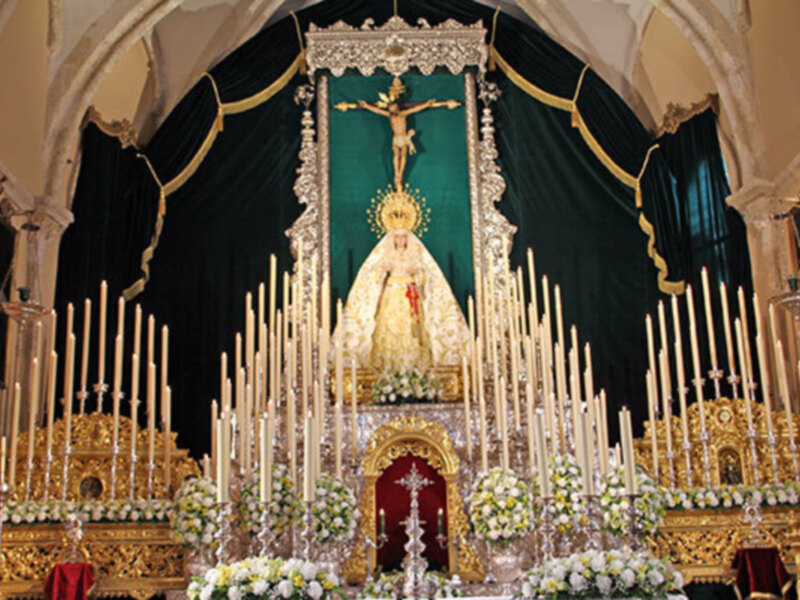 Altar ornado con velas, flores y estatua de la Virgen en un entorno religioso