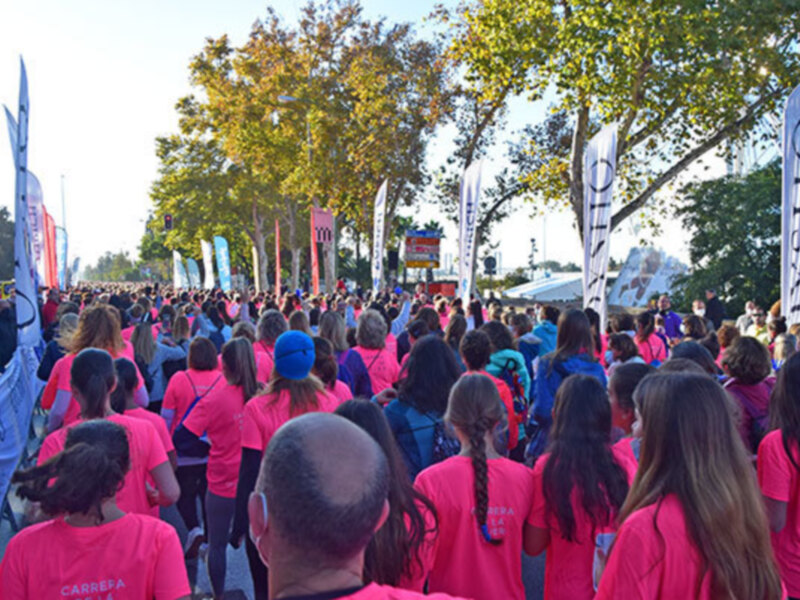 Carrera solidaria con participantes en camisetas rosas, celebrada en un parque con árboles y banderas.