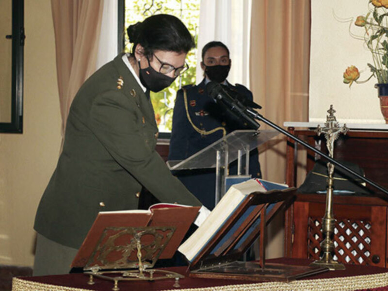 Oficial militar en uniforme y máscara hablando en un podium con un libro abierto en primer plano.