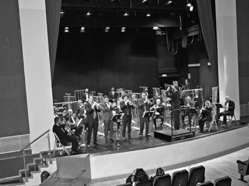 Orquesta de viento en escenario de teatro, en blanco y negro.