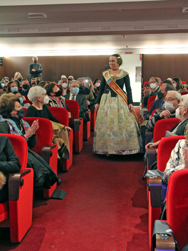 Una mujer en traje tradicional camina entre filas de asistentes en un auditorio.
