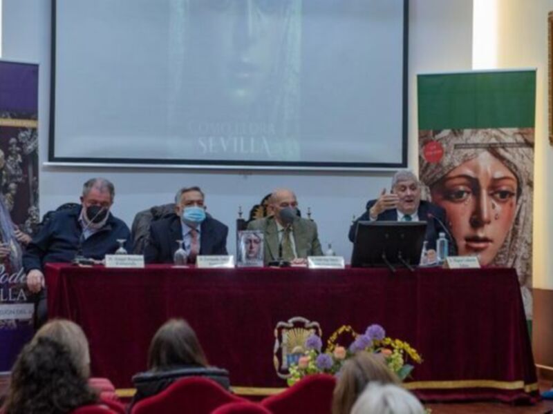 Conferencia de prensa en Sevilla sobre la Semana Santa, con personalidades en el escenario y público asistente en el fondo.