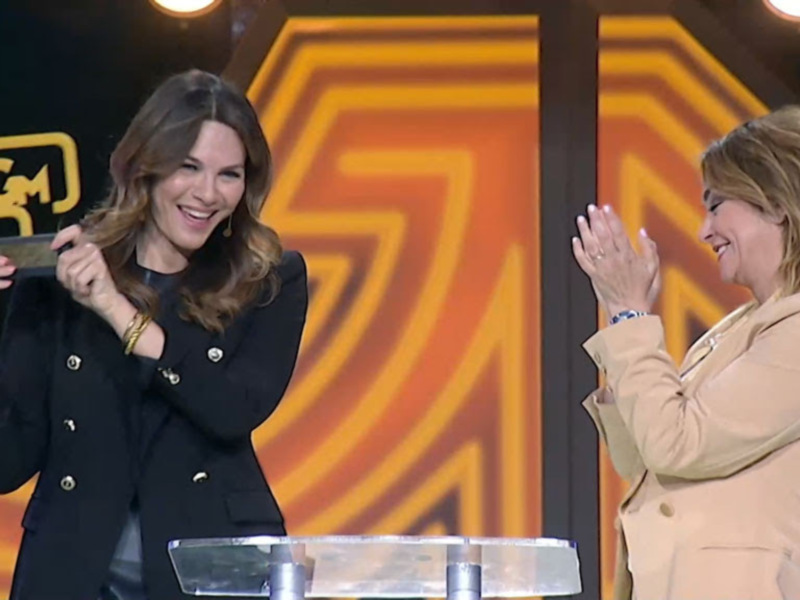 Dos mujeres en un escenario celebrando con aplausos y una tarjeta en mano.