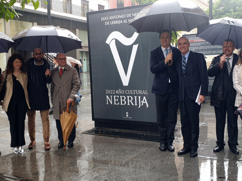 Celebración del Año Cultural 2022 en Lebrija bajo la lluvia, con autoridades y ciudadanos bajo paraguas.