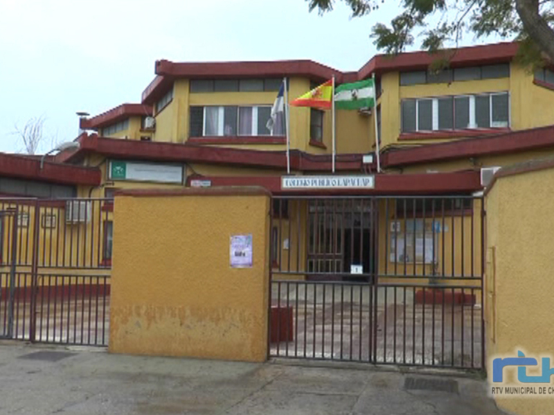 Fachada de un edificio amarillo con banderas en la parte superior y una puerta principal con barras metálicas. El edificio parece ser un centro administrativo o institucional.