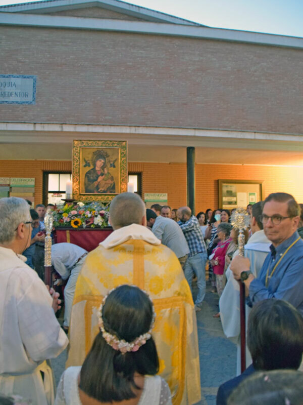 Procesión religiosa con imagen de la Virgen y fieles participando en una celebración en una iglesia.