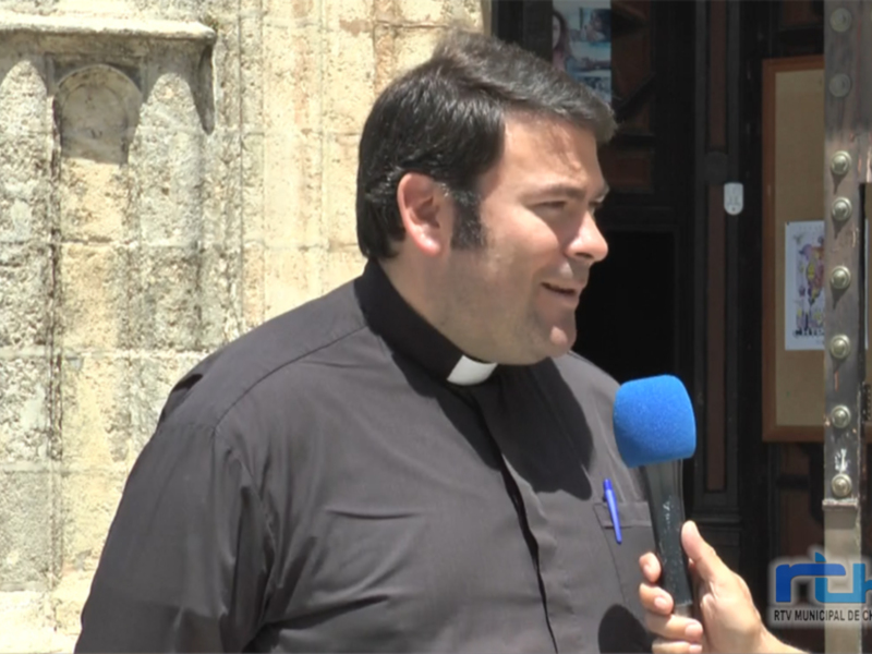Un sacerdote habla en una entrevista frente a un edificio histórico.