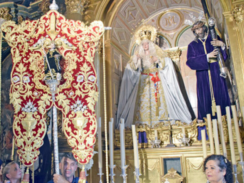 Procesión religiosa con estandartes y imágenes procesionales en un interior ornado de una iglesia.