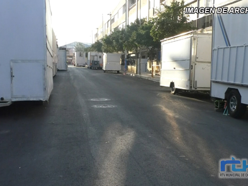 Vehículos de transporte en una calle industrial con edificios y árboles al fondo.