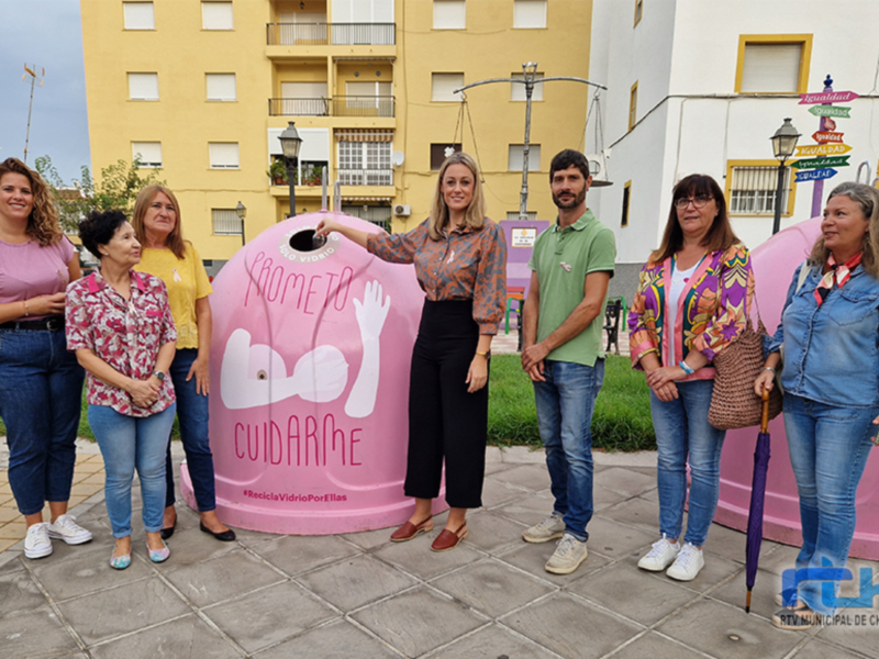 Grup de persones posant davant una caixa de reciclatge de vidre rosa amb el lema 'CUIDARME'.