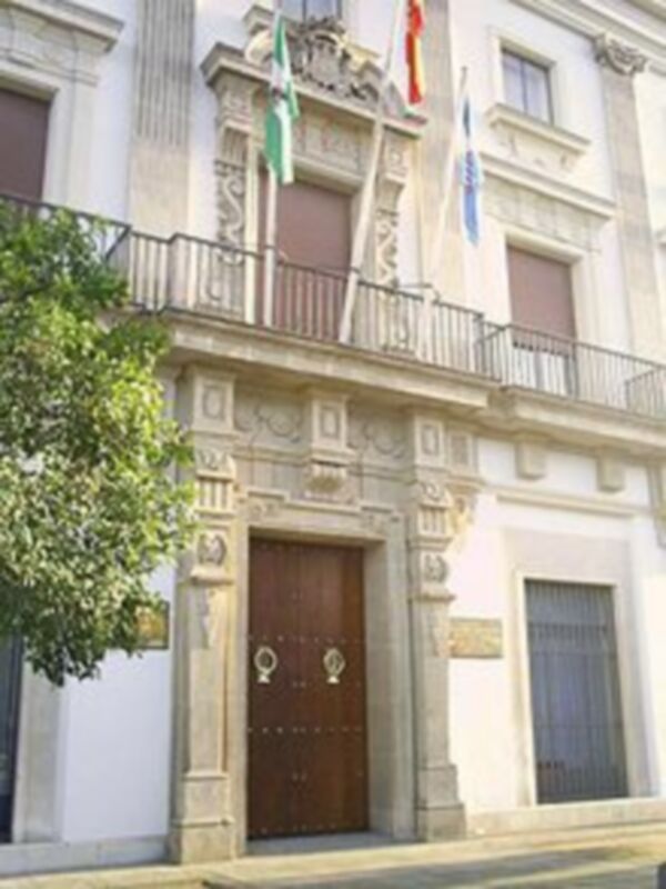 Fachada histórica de un edificio con detalles ornamentales y banderas en la parte superior.