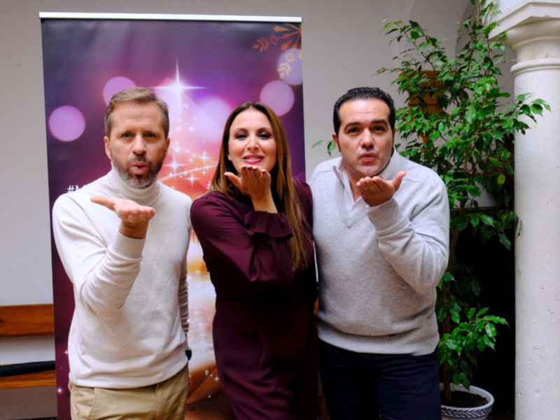 Tres personas saludando con las manos en un entorno acogedor con decoración navideña.