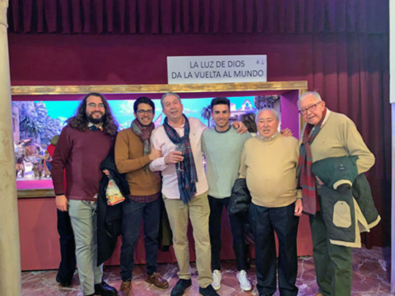 Grupo de personas posando juntos en un evento con una pancarta que dice 'La luz de Dios da la vuelta al mundo'.