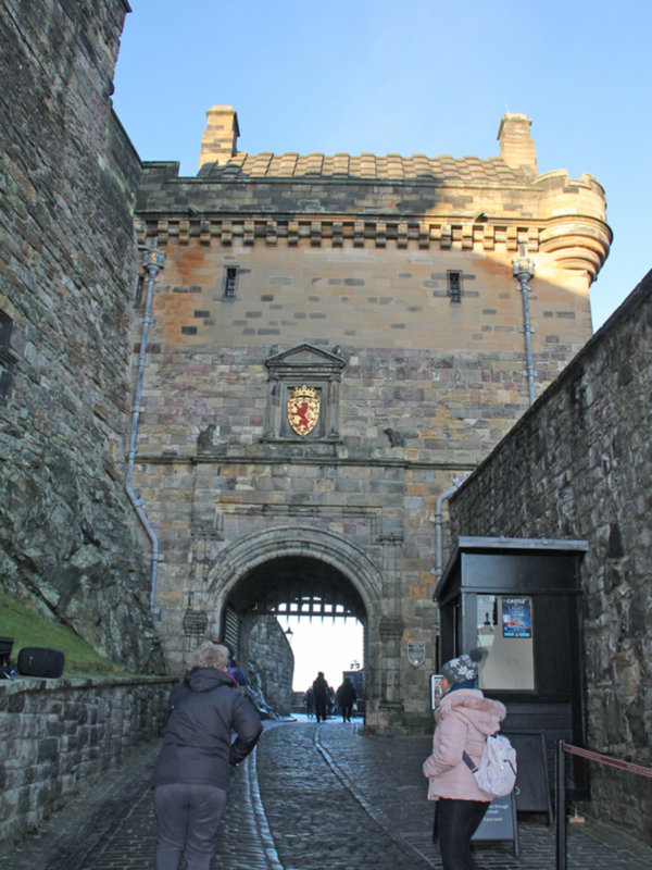 Puerta del castillo de Edimburgo, Escocia, con turistas explorando el recinto histórico.