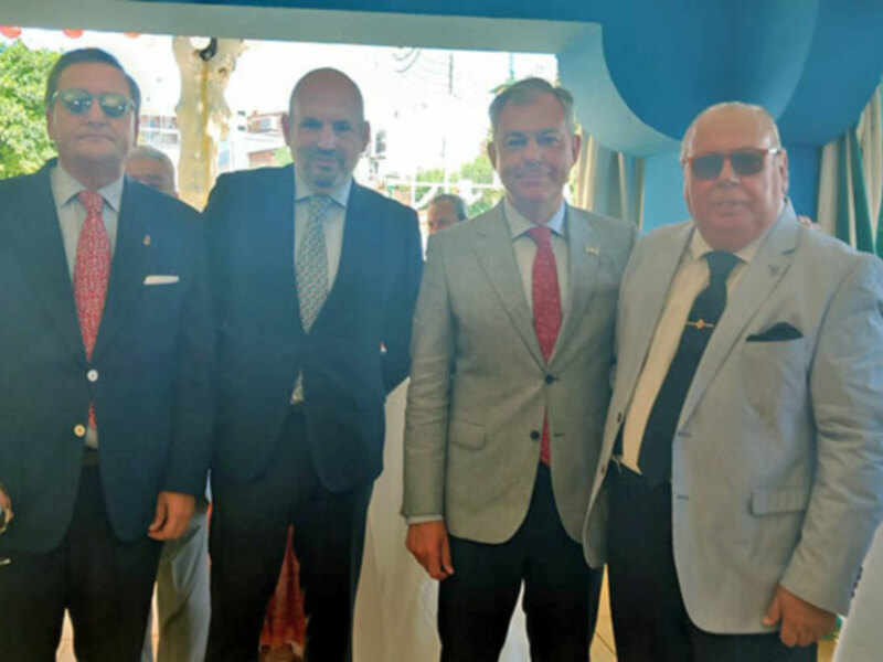 Cuatro hombres en trajes de negocios posan juntos en un evento formal al aire libre.