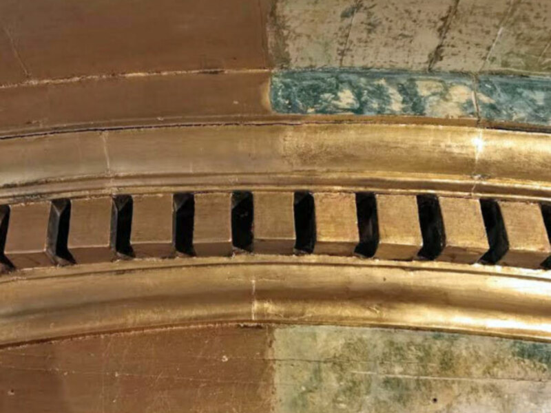 Detalle de un espejo antiguo con marco dorado y patrones decorativos en la parte superior.