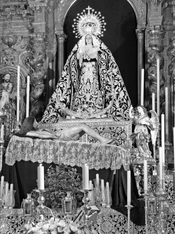 Representación de la Virgen María y el Niño Jesús en un altar con ornamentos y velas, en blanco y negro.