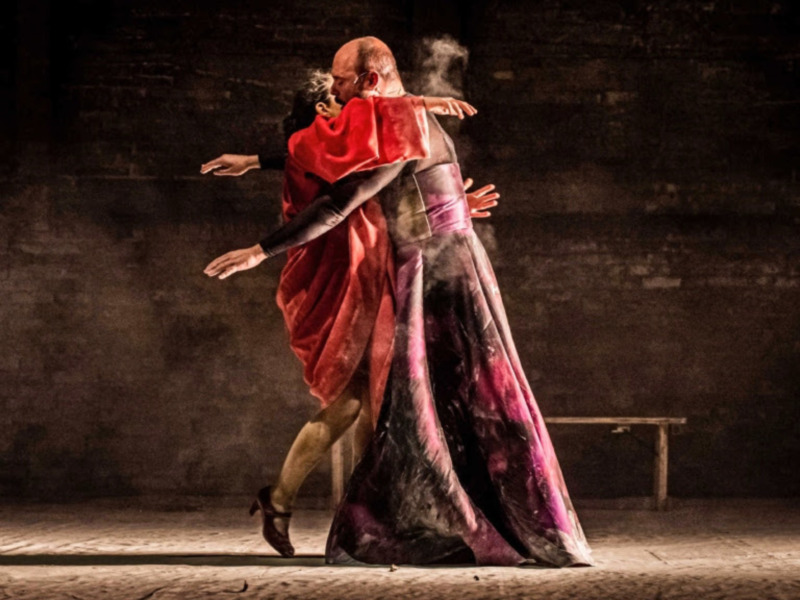 Danza contemporánea con vestimenta dramática y movimiento fluido en un escenario oscuro.