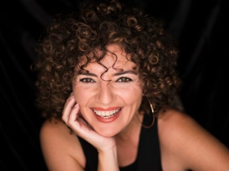 Retrato de mujer sonriente con cabello rizado, fondo oscuro