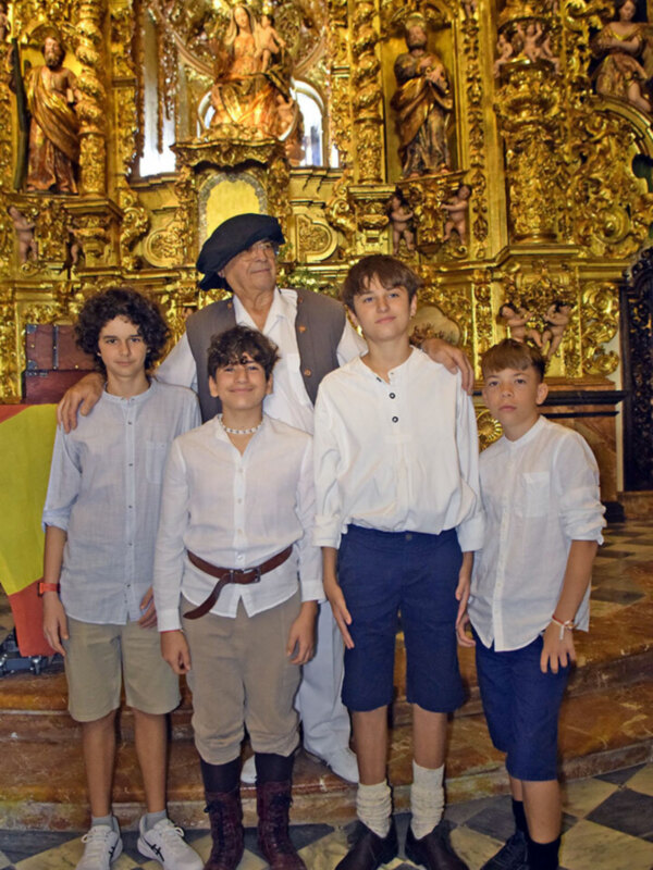 Un grupo de jóvenes y un adulto posan juntos en una iglesia con un fondo ornamental dorado y estatuas religiosas.