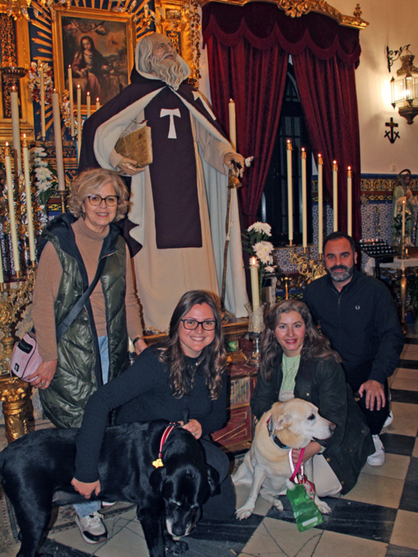 Grupo de personas y perros posando en frente de una estatua religiosa en un interior ornamental.