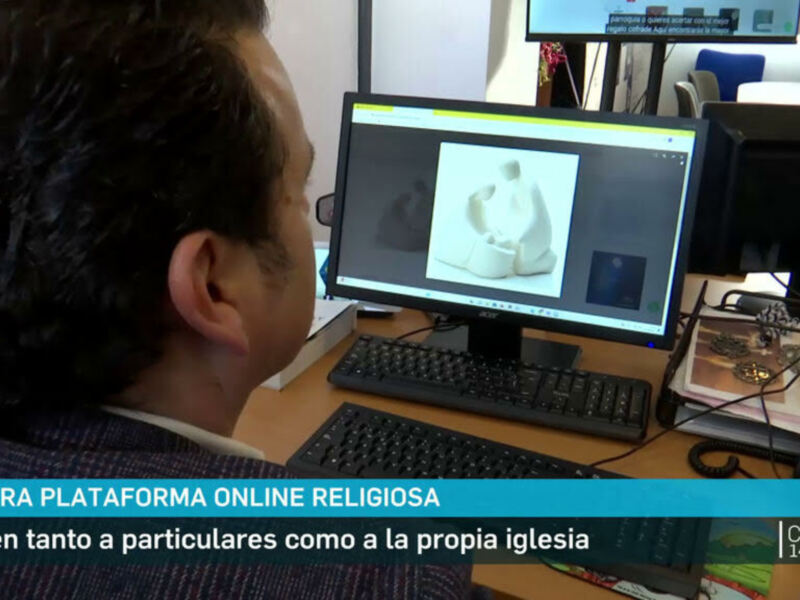 Un hombre trabaja en una computadora con una imagen de una estatua en la pantalla, en un entorno de oficina con dos monitores y un teléfono.