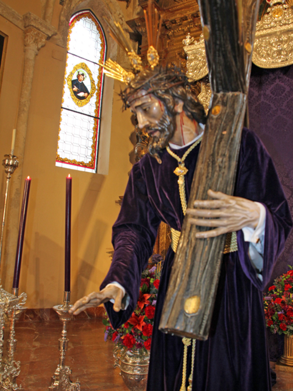 Estatua de Jesús Nazareno en un entorno religioso con velas y flores, representando la Semana Santa.